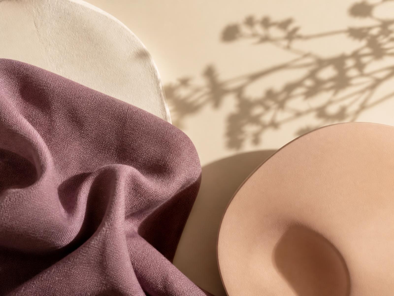 Softly lit ivory surface with a rounded pleasure product and folded linen